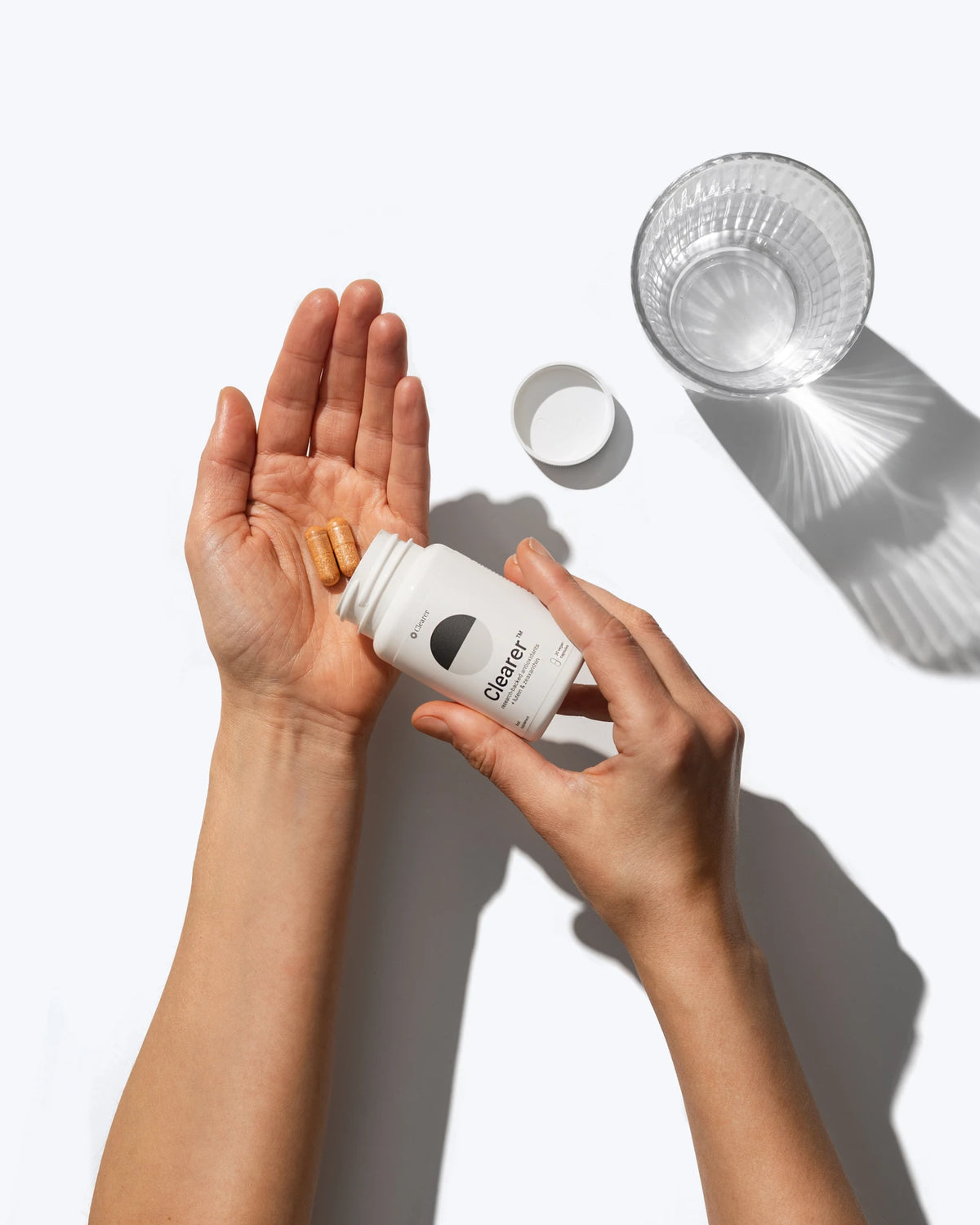 The Clearer daily routine: a capsule, an open bottle and a glass of water